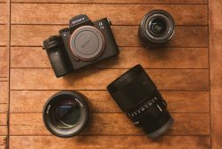 camera surrounded by sony lenses on wooden deck