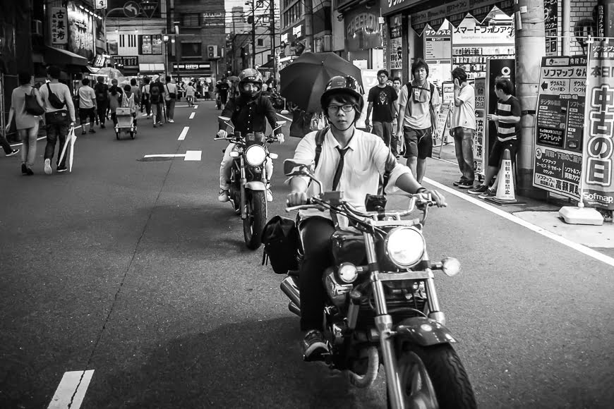 Black and white photo of a busy Japanese street with a man on a motor bike