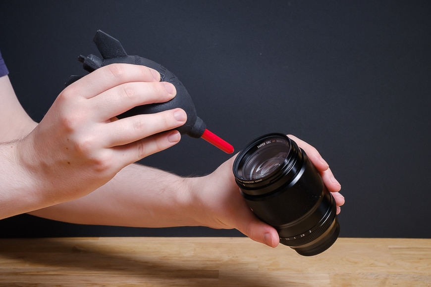 hands using blower on camera lens element